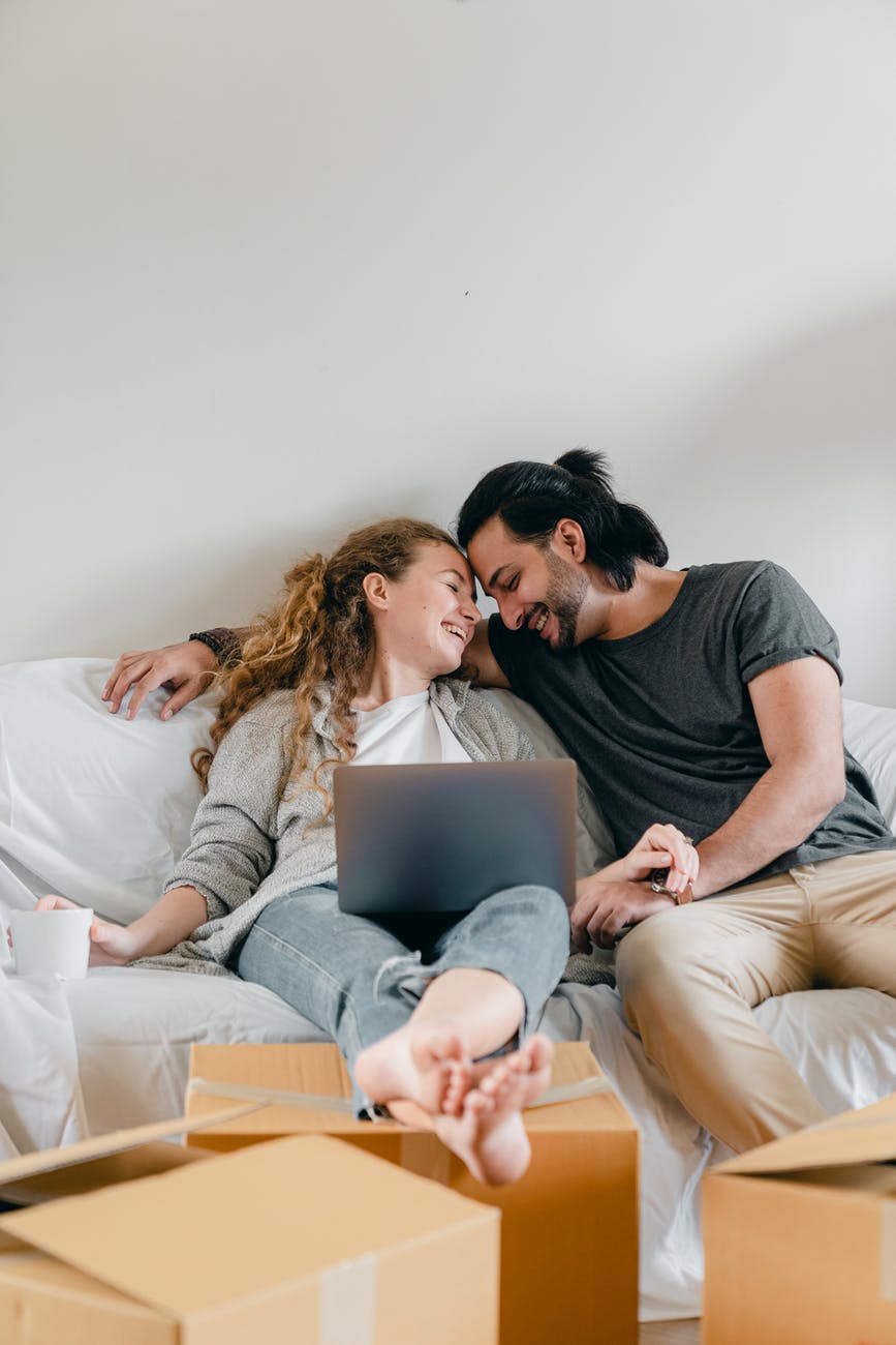 cheerful multiracial couple sitting on sofa with laptop at home